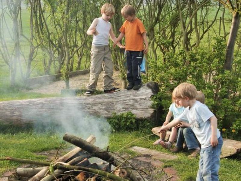 Kinder spielen draußen und machen Stockbrot am Lagerfeuer